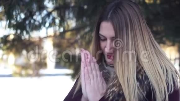 可爱的女孩在寒冷的天气里用嘴温暖她的手视频的预览图