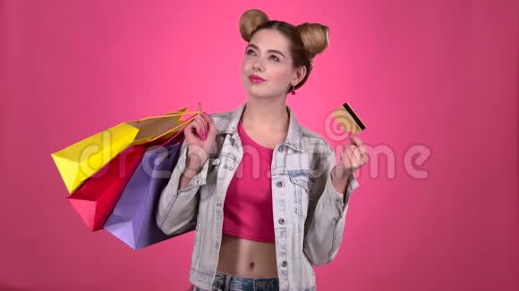 青少年拿着购物袋和一张金信用卡粉色背景慢动作视频的预览图