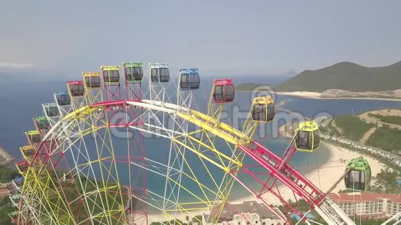 无人机在海上游乐园观赏五颜六色的摩天轮和青山景观大型摩天轮游乐园视频的预览图