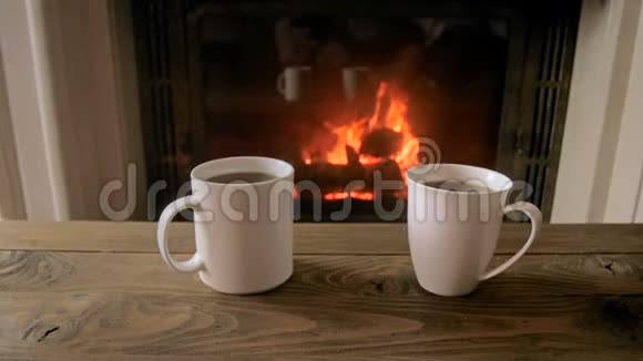 客厅有两个装有ot茶的杯子在燃烧的壁炉上的慢速镜头视频的预览图