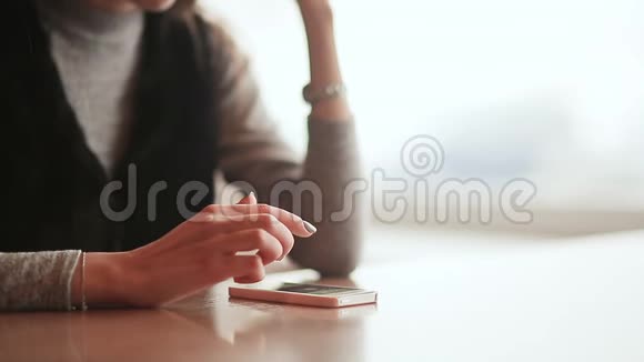 年轻漂亮的女孩手里拿着一部手机坐在咖啡馆的桌子旁休息一下女孩的手特写视频的预览图
