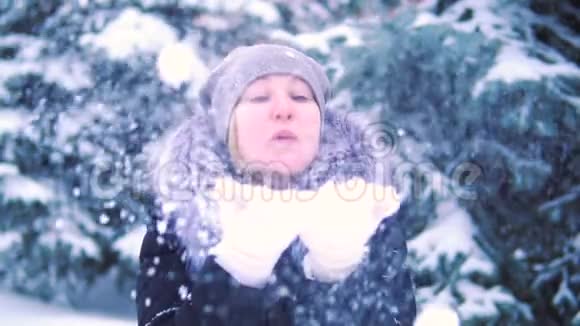 女孩在冬天的公园里用手吹雪慢镜头拍摄冬天的风景视频的预览图