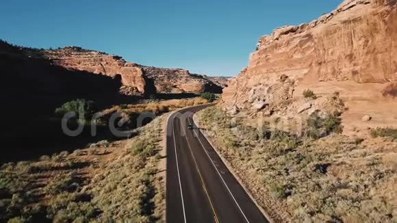 镜头跟随汽车行驶在高速公路上在大而陡峭的阳光峡谷山脉之间覆盖着沙子和岩石视频的预览图