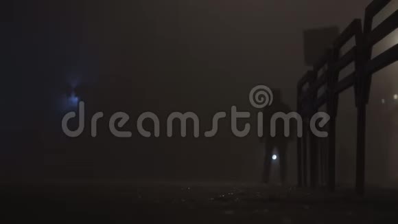 穿着夹克的人在夜间在雾中或雾中缓慢行走的路上的剪影视频的预览图