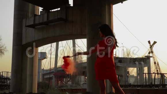美丽的女人穿着红裙子在废弃的桥下夕阳下翩翩起舞视频的预览图