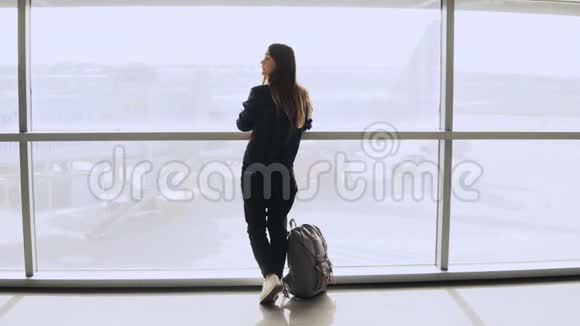 年轻女孩在机场窗口附近拍照带背包的快乐欧洲游客在终端使用智能手机4K视频的预览图