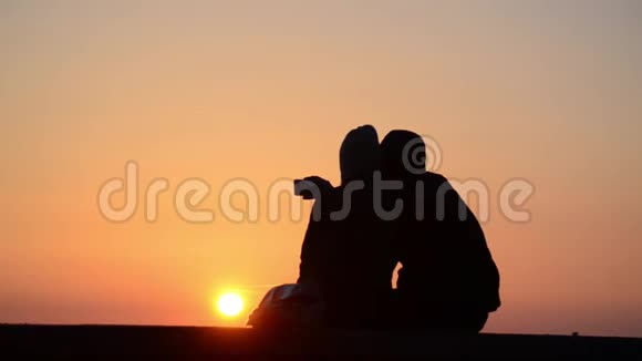 浪漫情侣在海上日落时相爱的剪影男孩和女孩享受日落和自拍与电话度假视频的预览图