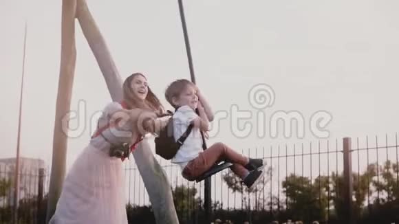 妈妈把儿子推到操场上的高空滑索上慢动作快乐男孩骑着一根长绳摆动拉链一家人在一起视频的预览图