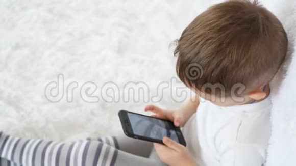 一个孩子喜欢在白色背景上玩手机拍他的腿特写镜头视频的预览图
