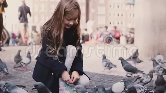 小白种人女孩坐在外面喂鸟慢动作快乐的女孩子在街上喂鸽子和平视频的预览图