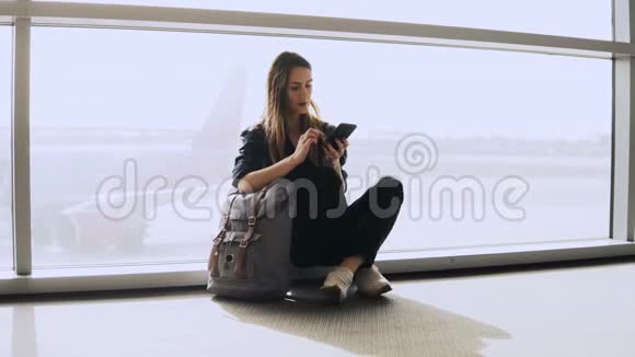 漂亮的女孩坐在终端窗口使用电话欧洲女乘客背包打字微笑快乐4K视频的预览图
