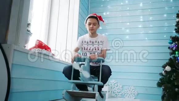 一个戴着圣诞老人帽子少年坐在儿童摇椅上视频的预览图