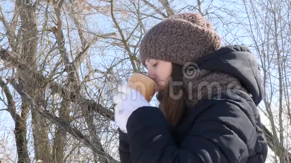 女人喝热茶或咖啡从一个舒适的杯在雪冬早户外美丽的女孩享受冬天视频的预览图