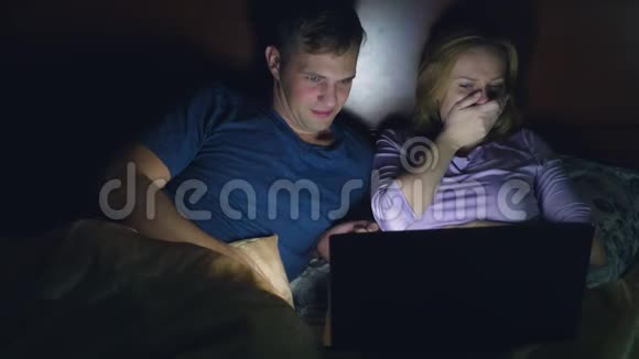 夫妻男人和女人在睡觉前在卧室的床上用笔记本电脑看电影看恐怖电影观众视频的预览图