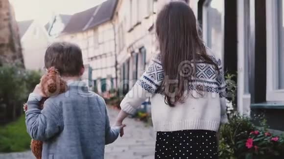 镜头跟随两个小孩子手牵着手走着慢动作后视女孩和男孩在老城闲逛兄弟姐妹视频的预览图