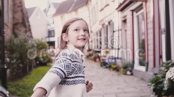 小女孩看着镜头在铺好的路上奔跑后景慢动作可爱的欧洲孩子在老街上跑步视频的预览图