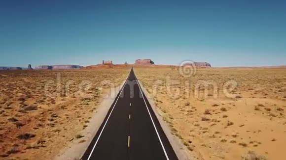 无人机跟随汽车沿着标志性的美国沙漠公路公路在纪念碑谷与大悬崖山脉天际线视频的预览图