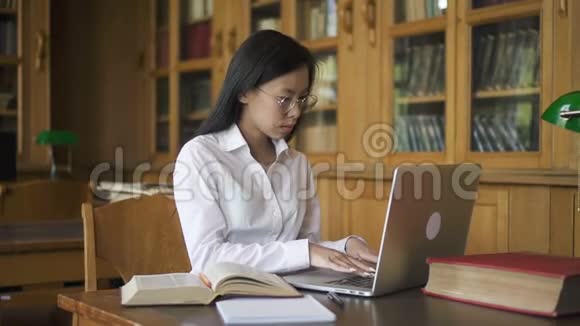 漂亮的女人正在使用笔记本电脑看书坐在图书馆的桌子上视频的预览图