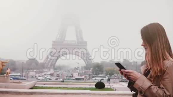 法国巴黎埃菲尔铁塔附近站着的年轻快乐女人的肖像使用智能手机慢动作视频的预览图