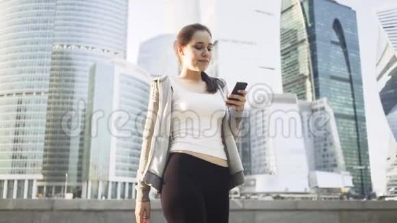 微笑的年轻女子在莫斯科的一条街上看着她的智能手机视频的预览图