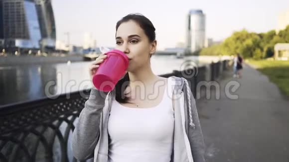 微笑的年轻女子穿着运动服喝着水在莫斯科市散步视频的预览图