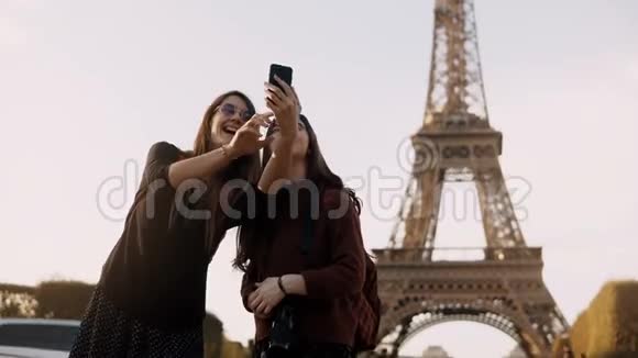 两位美丽的旅行女性在阳光明媚的日子在法国巴黎埃菲尔铁塔附近的智能手机上拍照视频的预览图