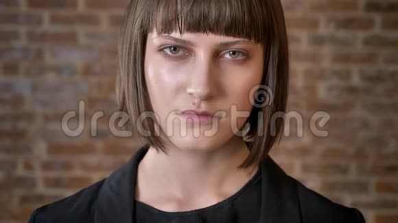 严肃的年轻女性剪短头发看着摄像机在砖背景上被隔离视频的预览图