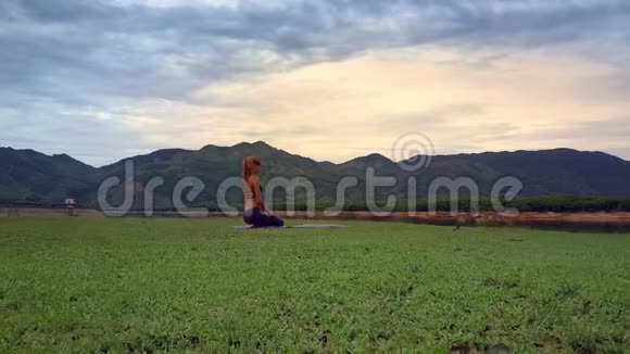 从坐在湖岸瑜伽姿势的女孩身上取下飞行摄像机视频的预览图