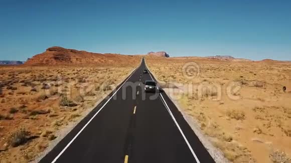 无人机跟随两辆汽车沿着美丽的公路公路行驶纪念碑谷宽阔开阔一望无际的干燥沙漠景观视频的预览图