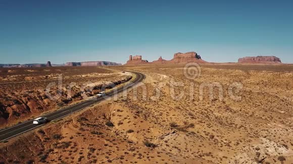 汽车通过无人机相机在沙漠公路道路上阳光明媚的纪念碑谷在美国惊人的平坦的山脉天际线视频的预览图