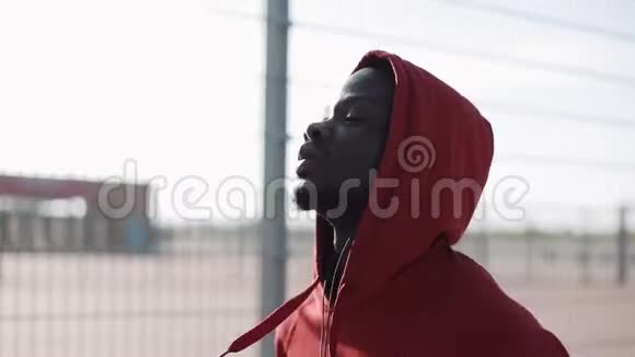 在城市日落时奔跑的人穿红色连帽衫的非裔美国男运动员户外健身运动视频的预览图