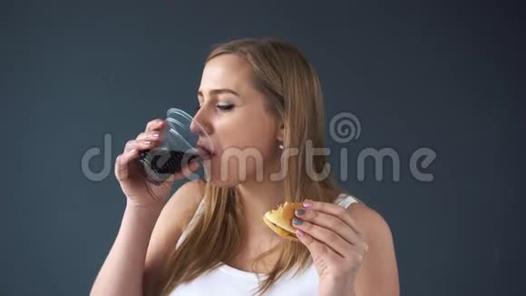 超重的女人在灰色背景下吃汉堡包喝汽水摄像机向下移动显示视频的预览图