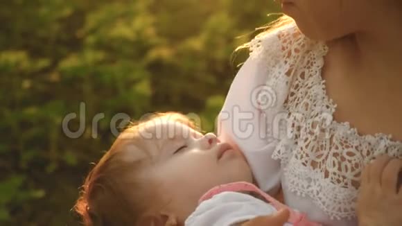 一个小孩子抱着妈妈睡着了母女俩正走在夏天的公园里慢镜头视频的预览图