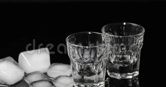 将伏特加倒入装有冰块的杯中置于黑色背景下视频的预览图