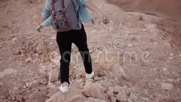女孩走在沙漠的陡坡上慢动作年轻女子在巨大的裂口岩石和石头上徘徊危险的道路视频的预览图