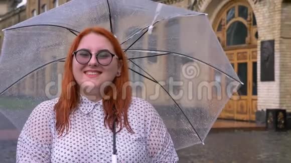 戴眼镜的胖姜女站在雨天撑着伞看着镜头微笑着继续前进视频的预览图