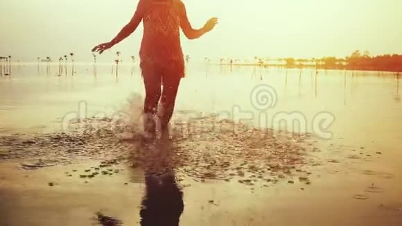 在美丽的夕阳下穿着短裙的年轻女子在海滩上奔跑慢动作1920x1080高清视频的预览图