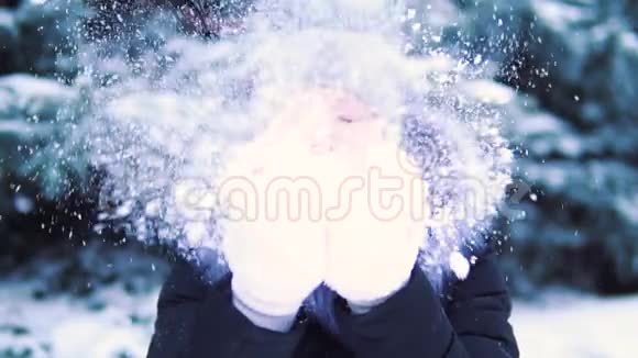 缓慢的动作女孩在手掌上吹雪在白雪覆盖的冬季公园里微笑和欢乐视频的预览图