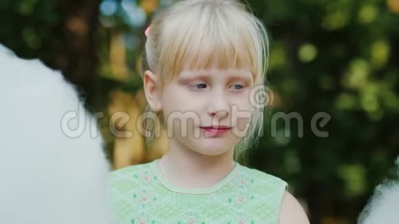 酷的金发女孩6岁正在公园里吃甜棉毛景深较浅的肖像视频的预览图