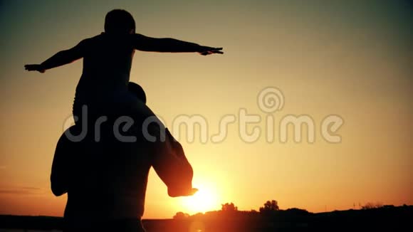 父亲和儿子在海滩上玩耍的剪影男孩举起双手在美妙的日落中模仿飞行视频的预览图