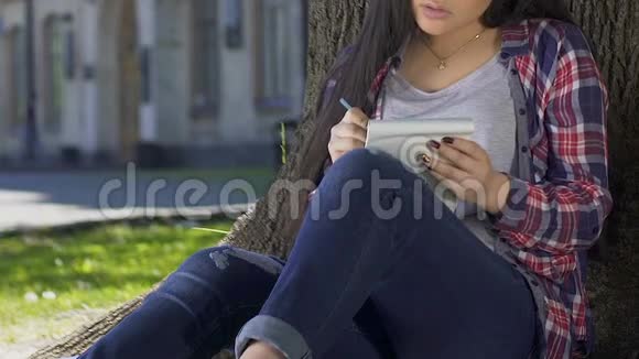 浪漫的女孩写爱情诗坐在夏日公园的大树影里视频的预览图