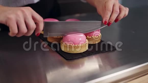 女人手在厨房的工作表面上用粉红色的镜面釉切割法国甜点粉色蛋糕近景视频的预览图