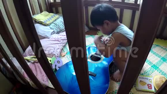 2岁的小男孩好奇在婴儿床上弹奏吉他视频的预览图