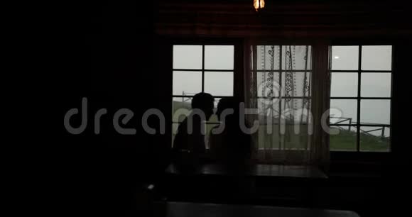 一对接吻情侣坐在山上某处黑房子的窗户前的剪影视频的预览图