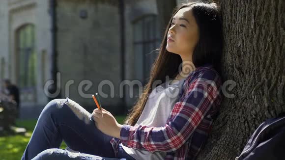 在温暖的阳光下坐在树下寻找灵感的混血女孩视频的预览图