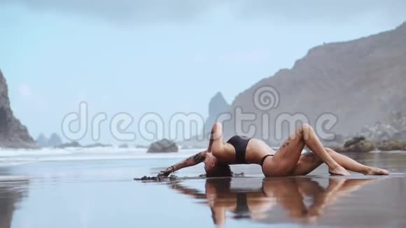 女人在靠近大海的沙滩上在群山和黑沙上翩翩起舞视频的预览图