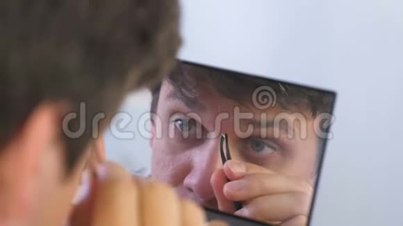 年轻人用镊子在家里的镜子前拔掉眉毛视频的预览图
