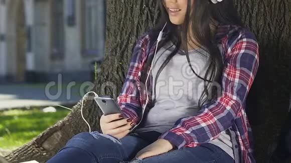 可爱的女孩在耳机里享受音乐在智能手机上浏览网页视频的预览图