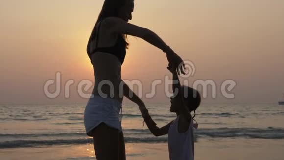 日落时分年轻母亲和小女儿在沙滩上跳舞的剪影视频的预览图