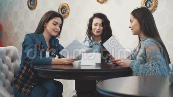快乐的三个漂亮女孩和她们的女朋友坐在咖啡馆里在此期间讲述和讲述各种故事视频的预览图